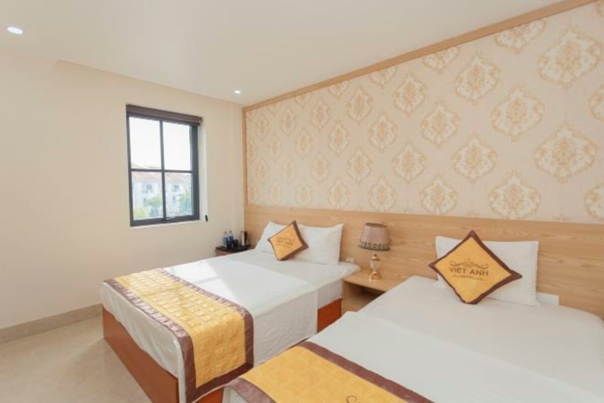 A hotel room with two single beds, a nightstand with a lamp, and a window with a view.