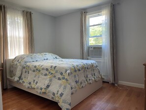 A bedroom with a bed, a window with curtains, and an air conditioning unit.