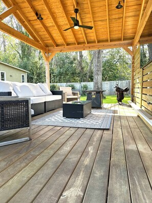 Una terraza exterior con suelo de madera, ventilador de techo y zona de estar con sofá y mesa.