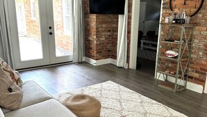 A living room with a sofa, ottomans, a clock, and a brick wall.