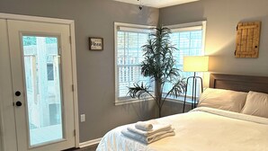 A bedroom with a bed, a ceiling fan, a window with blinds, a potted plant, and a door with a glass panel.