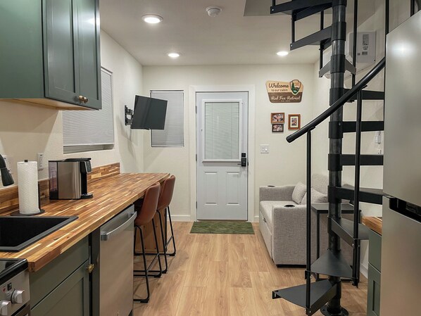 A compact kitchen with a wooden countertop, a built-in coffee machine, and a small dining area with stools.