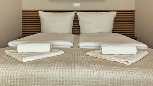 Uma cama bem arrumada com lençóis brancos, duas almofadas e toalhas dobradas.