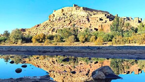 A desert landscape with a rocky hill and a body of water reflecting the scene. - Dar INNA  (Ait Benhaddou)