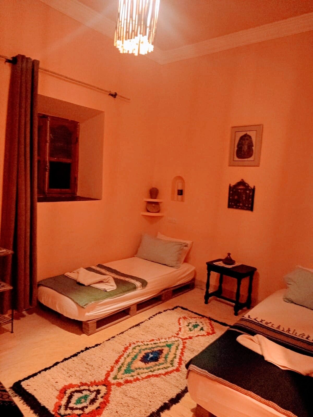 Un dormitorio pequeño y acogedor con una cama individual, una mesita de noche, un estante pequeño y una ventana con cortinas.