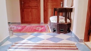 A hallway with a checkered floor, a striped rug, and a wooden chair. - Dar INNA  (Ait Benhaddou)