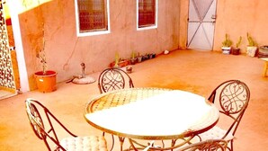 An outdoor patio with a round table and four chairs. There are potted plants and a gate in the background. - Dar INNA  (Ait Benhaddou)