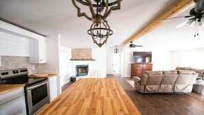 Une cuisine spacieuse avec un îlot central en bois, des meubles blancs et un four encastré. On y trouve également un coin repas avec un canapé et un téléviseur en arrière-plan.