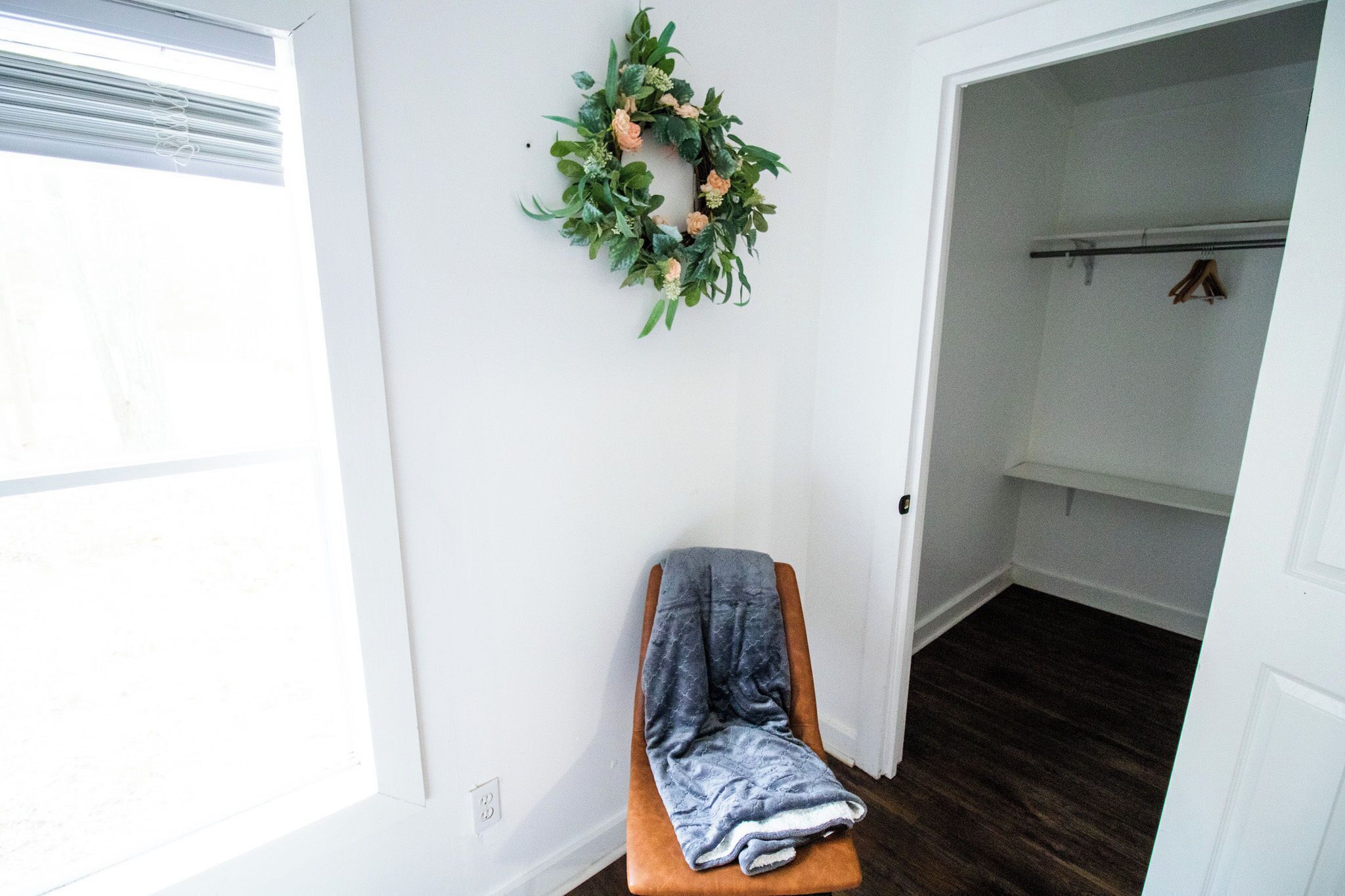 A room with a bench, a door leading to a closet, and a wall-mounted wreath.