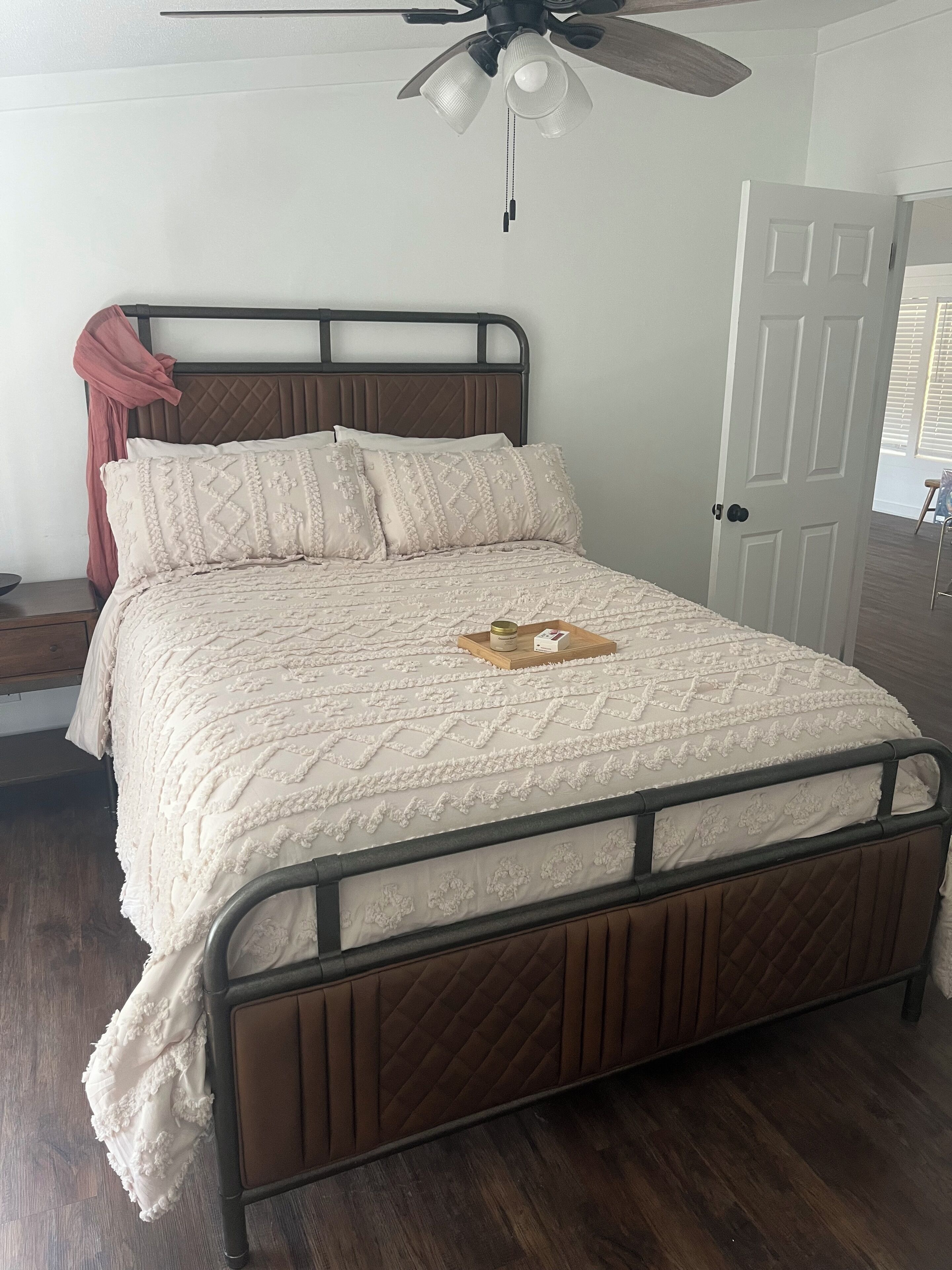 A bed with a quilted headboard, a wooden nightstand, and a ceiling fan.
