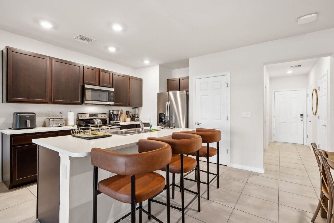 A modern kitchen with dark wooden cabinets, stainless steel appliances, and a white island with bar stools.