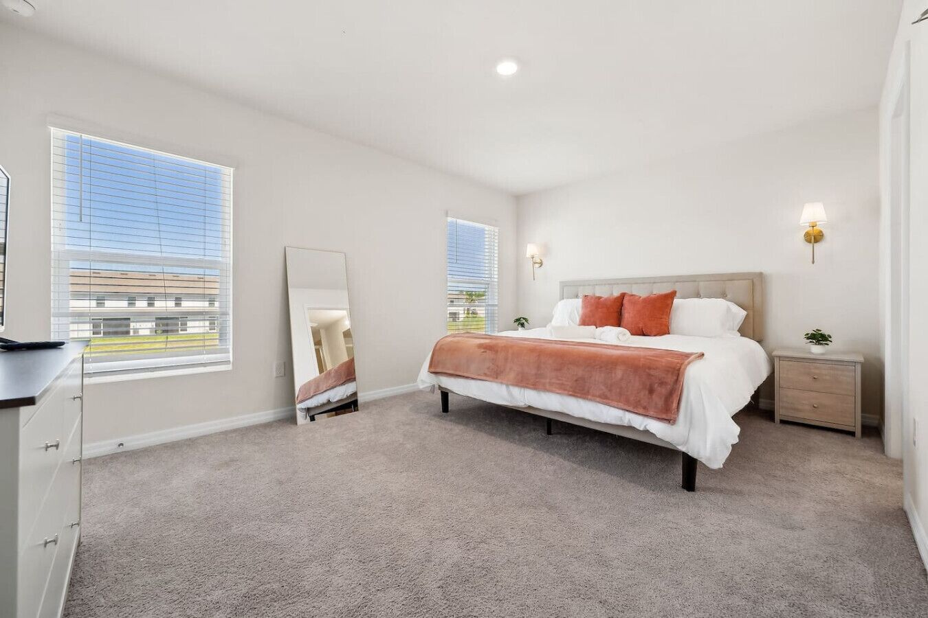 A bedroom with a bed, bedside tables, a mirror, and a window.
