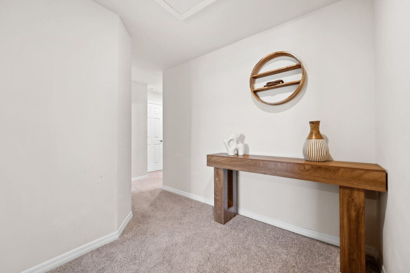 A hallway with a wooden console table, a round mirror, and two vases.