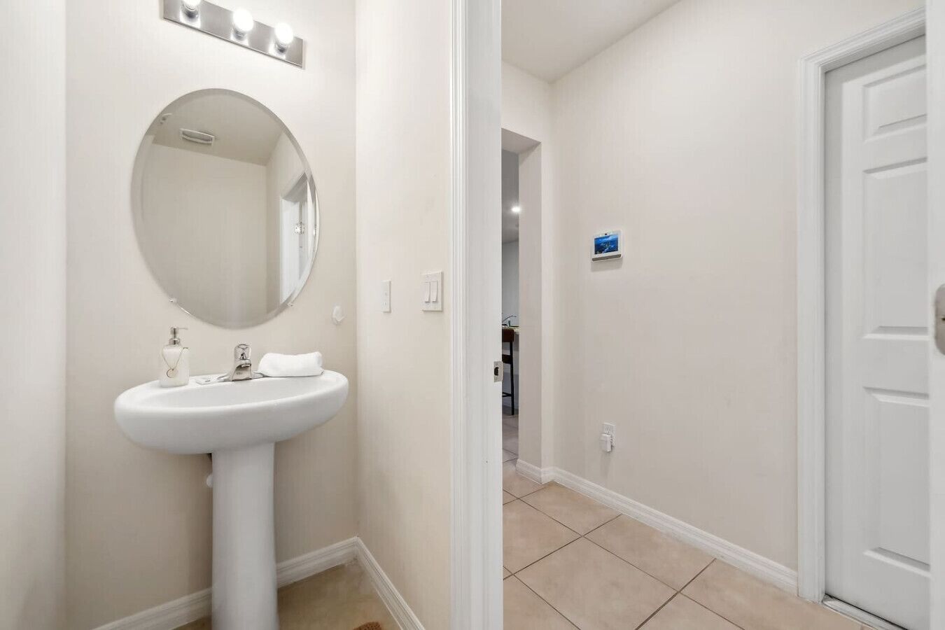 Une salle de bain avec un miroir rond, un lavabo sur colonne et une petite étagère contenant des articles de toilette.