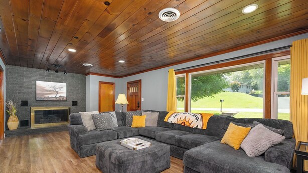 Sala de estar com lareira, sofá seccional e uma grande janela com vista para uma paisagem verde.
