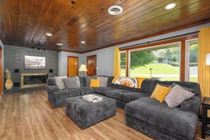 A living room with a fireplace, a sectional sofa, and a large window with a view of a green landscape. - Minutes Away from Downtown Bristol & the Speedway (Bristol)