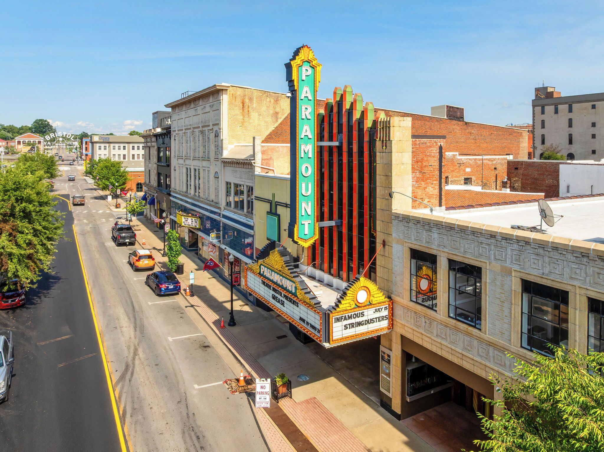 A street view with a Paramount theater featuring a marquee advertising 'INFAMOUS STRINGDUSTERS.'