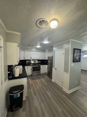 A spacious kitchen with white cabinets, stainless steel appliances, and a black countertop. - Charming 3-bedroom house with WiFi and AC in Hollandale (Hollandale)