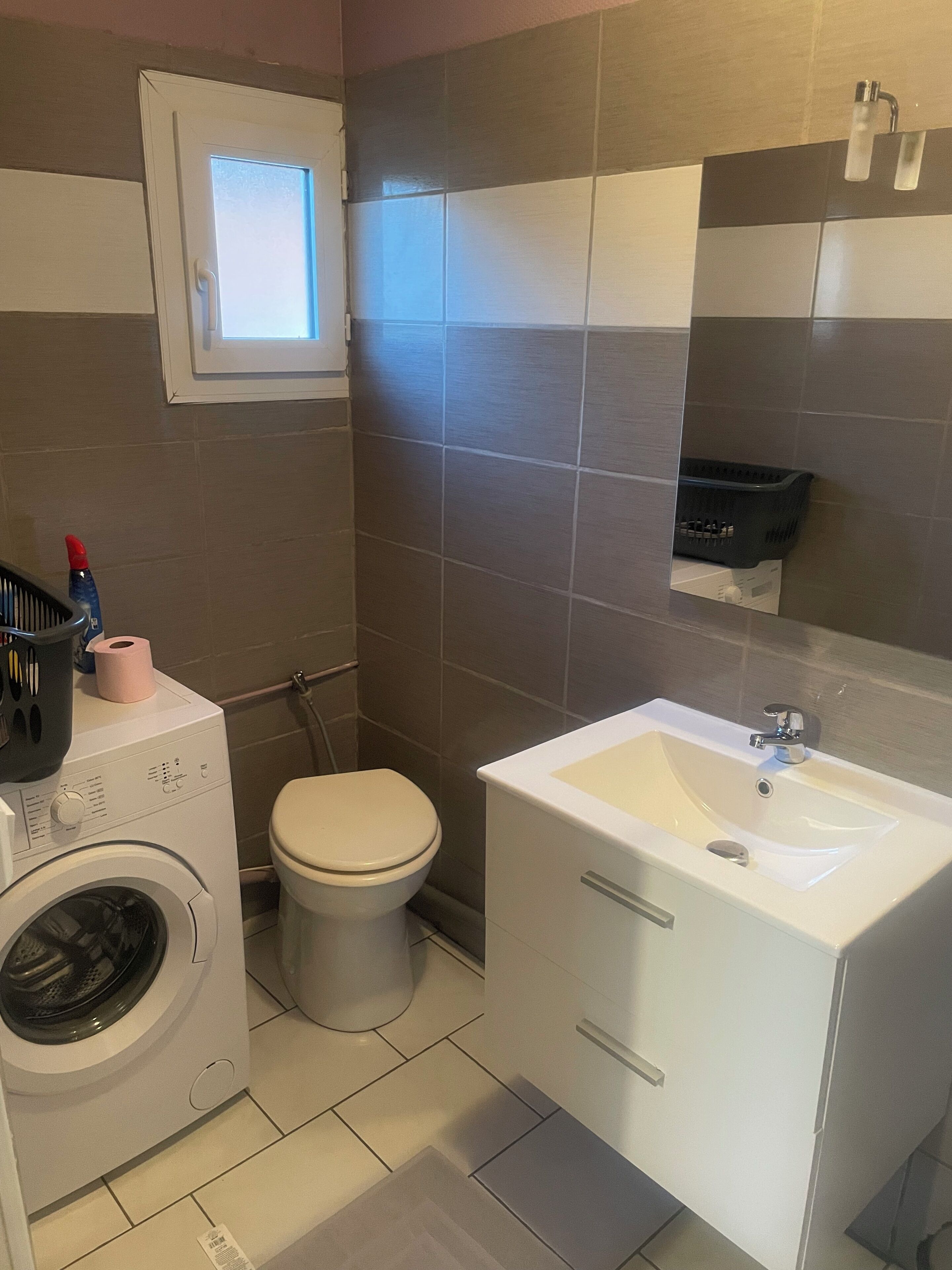 A compact bathroom with a washing machine, toilet, and sink.