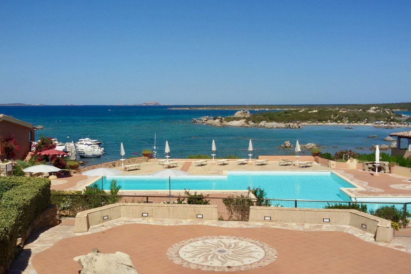 A pool area with a view of the sea, lounge chairs, umbrellas, and a decorative tile pattern.