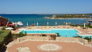Un espace piscine doté de chaises longues et de parasols, avec vue sur une plage et la mer.