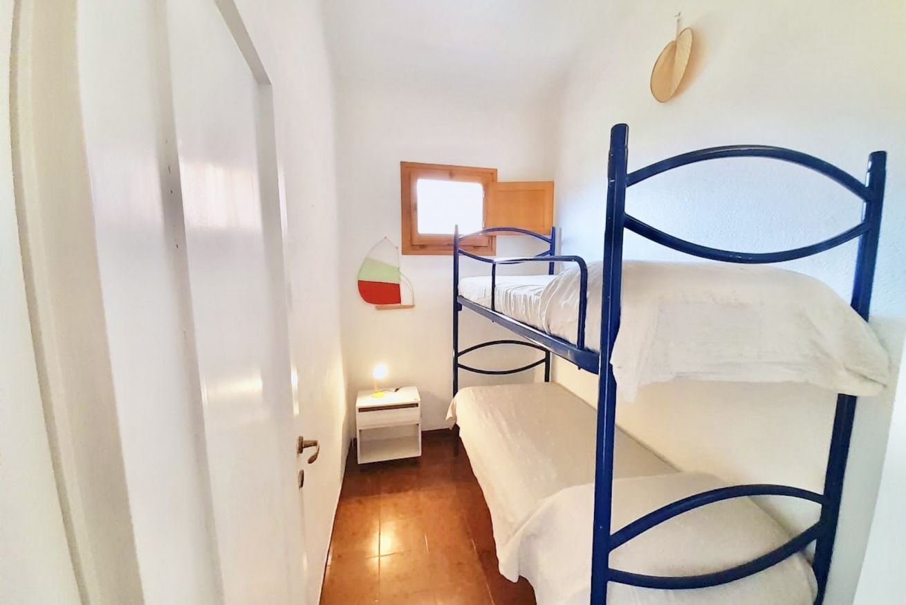 A dormitory room with bunk beds, a small bedside table with a lamp, and a window with a wooden frame.