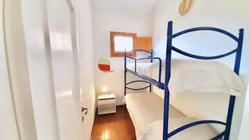 A dormitory room with bunk beds, a small bedside table with a lamp, and a window with a wooden frame.
