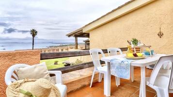 An outdoor patio with a table and chairs, a hat, and a view of the sea.