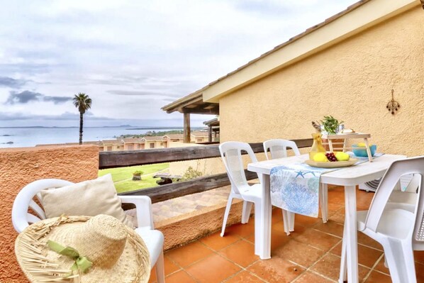Un patio exterior con una mesa, sillas, un sombrero y vistas al mar.