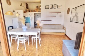 Un comedor con mesa y sillas blancas, un sofá y una cocina al fondo.