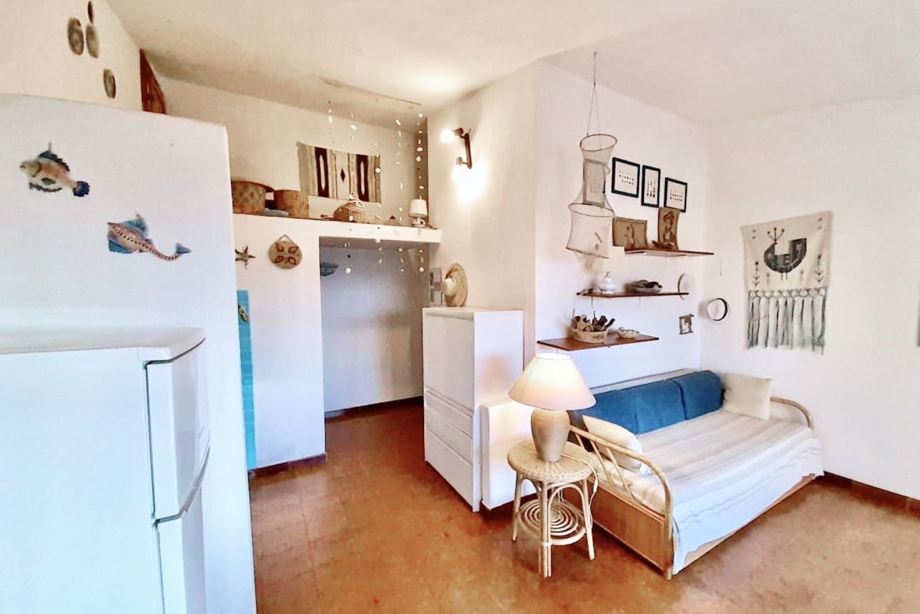 Un espace de vie compact comprenant un coin cuisine, un canapé, une petite table et des éléments de décoration murale.