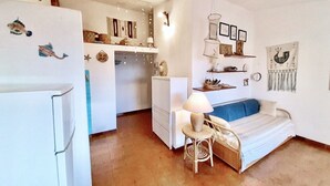 Un espace de vie compact comprenant un coin cuisine, un canapé, une petite table et des éléments de décoration murale.