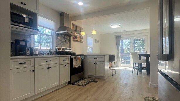 Una cocina moderna con armarios blancos, horno empotrado y comedor con mesa y sillas.