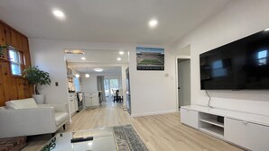 Una sala de estar moderna con un televisor de pantalla plana, una mesa de centro de vidrio y una zona de estar con sofás blancos.