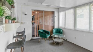 Una habitación con una mesa de vidrio, dos sillas verdes, una silla gris, una puerta blanca y una ventana con persianas.