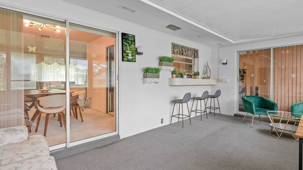 Un interior moderno con una zona de comedor, una barra con taburetes y un sillón verde.