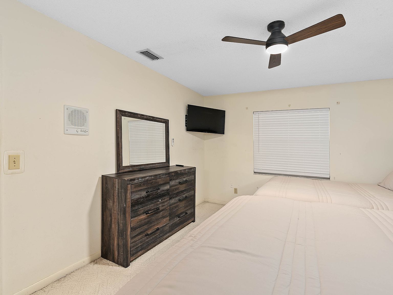 A bedroom with a bed, dresser, ceiling fan, TV, and window blinds.