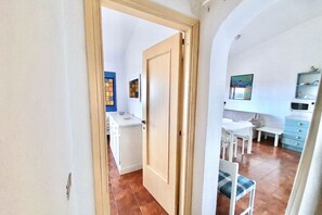 A room with a wooden door, a dining area with a table and chairs, and a kitchen area with a microwave and cabinets.