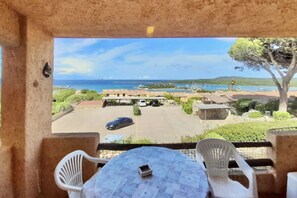 A balcony with a view of the sea, a parking area, and a table with chairs.