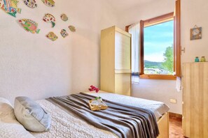 Une chambre à coucher avec un lit, une fenêtre donnant sur un beau paysage, une armoire en bois et des décorations murales représentant des poissons.