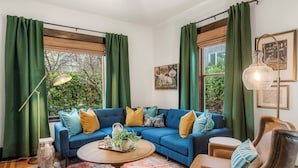 A living room with a blue sofa, green curtains, and a coffee table. - Game Room, Fire Pit, Sleeps 12, Walkable Retreat (Seattle)