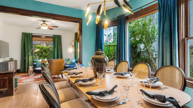 A dining area with a wooden table set for a meal, surrounded by chairs, and a view of greenery outside. - Game Room, Fire Pit, Sleeps 12, Walkable Retreat (Seattle)