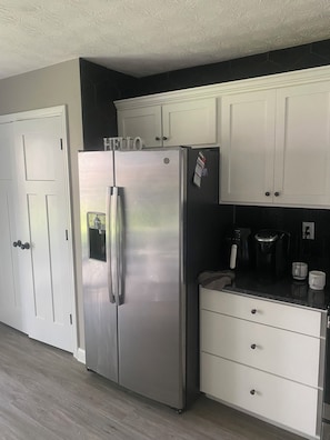 A kitchen with a stainless steel refrigerator, white cabinets, a coffee maker, and a microwave.