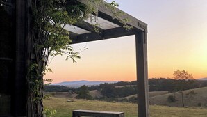 Une pergola en bois avec un banc donnant sur un paysage rural au coucher du soleil.