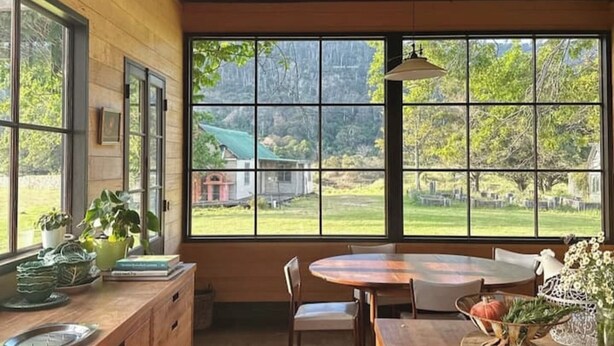 Une cuisine avec des poutres en bois, de grandes fenêtres et une vue sur un paysage verdoyant.
