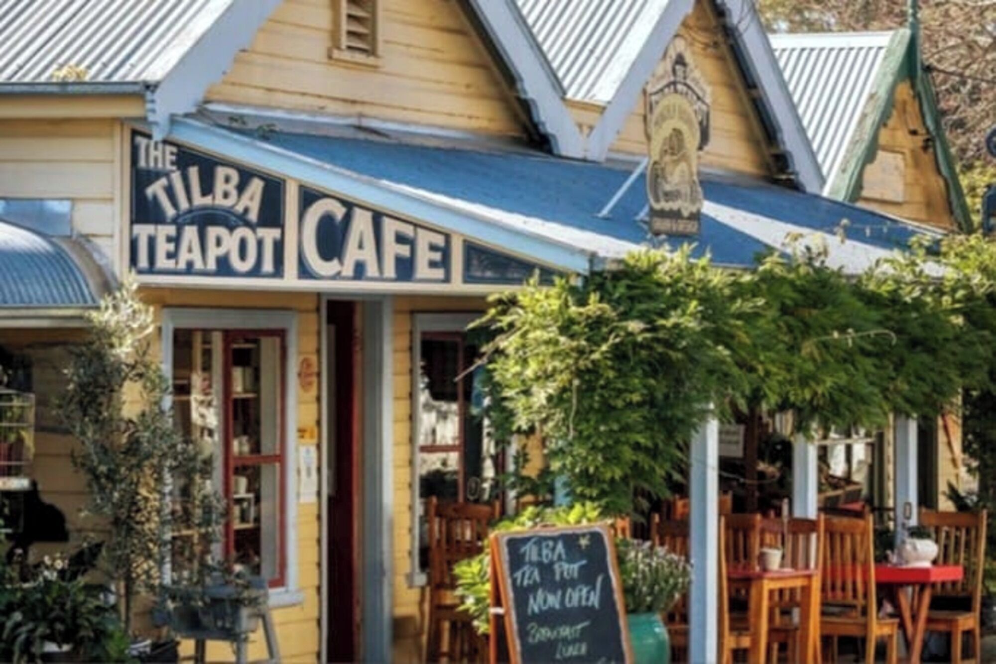 The exterior of The Tilba Teapot Cafe with a sign indicating it is now open.
