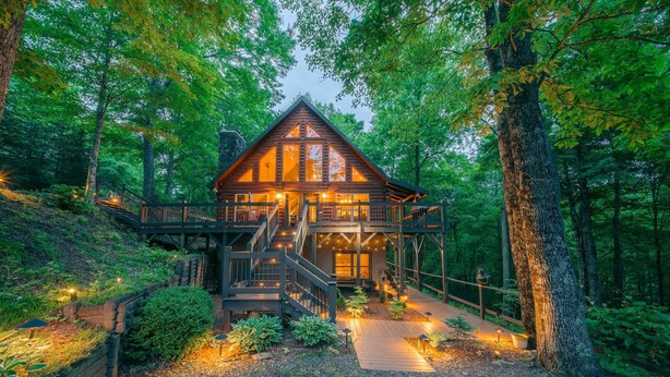 A cabin with a wooden exterior, a deck, and a staircase leading to the entrance. - Modern Log Cabin with all the Amenities (Todd)