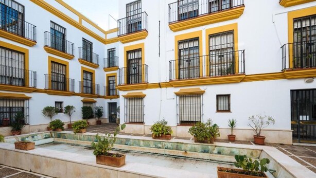 A courtyard with white buildings, yellow trim, and potted plants. - Bellas Artes I in Sevilla (Seville)