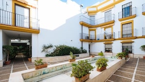 A courtyard with potted plants, a tiled floor, and a white building with yellow trim and balconies. - Bellas Artes I in Sevilla (Seville)