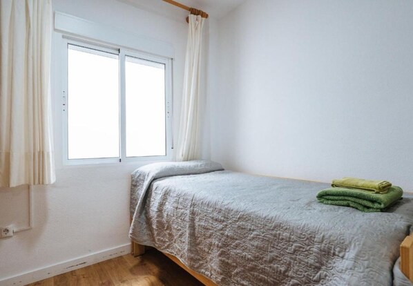 A small, single-bed room with a window, a bed with a grey patterned bedspread, and a green towel on the bed. - Bellas Artes I in Sevilla (Seville)